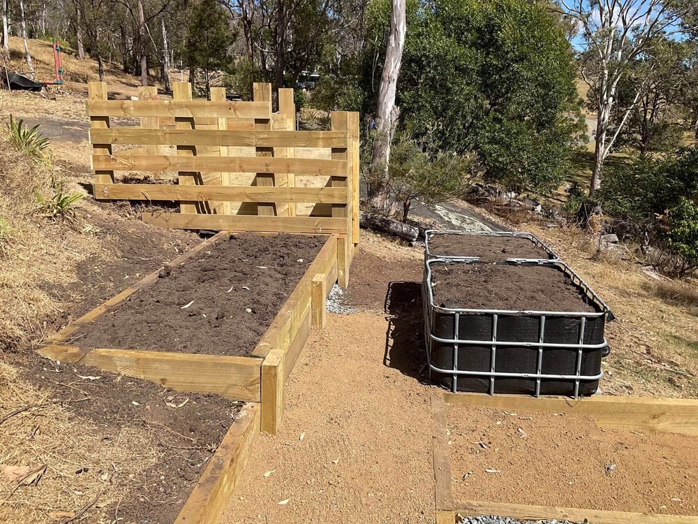 An IBC wicking bed set into a freshly landscaped slope, alongside timber retaining walls and a raised garden bed
