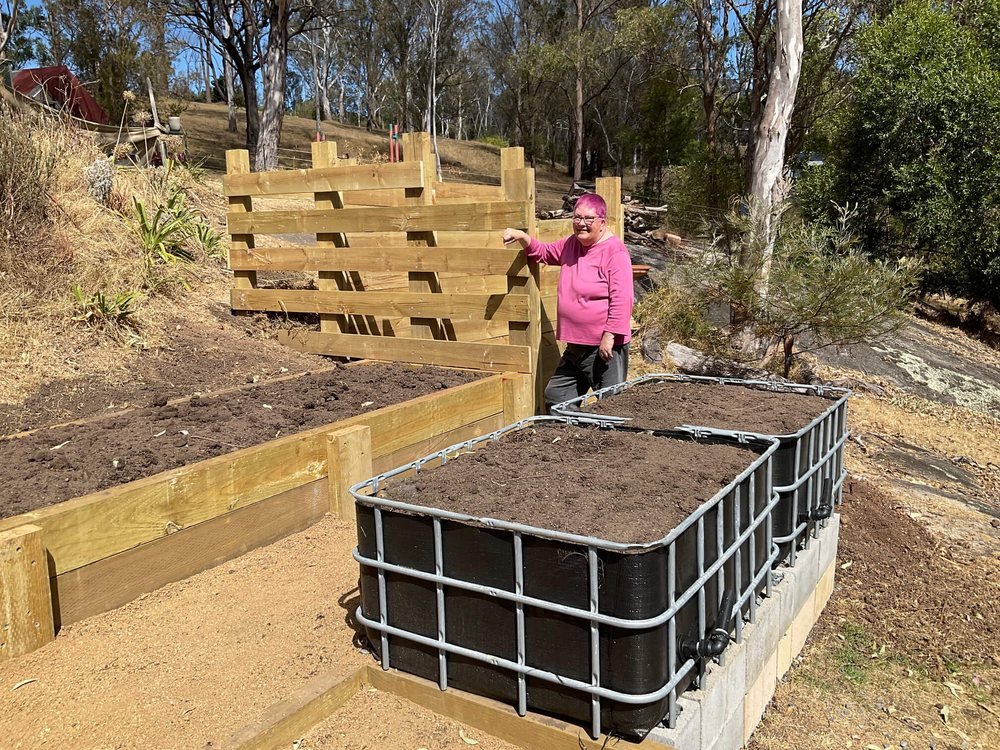 A finished IBC wicking bed on a landscaped garden terrace, with the gardener standing by the timber retaining wall