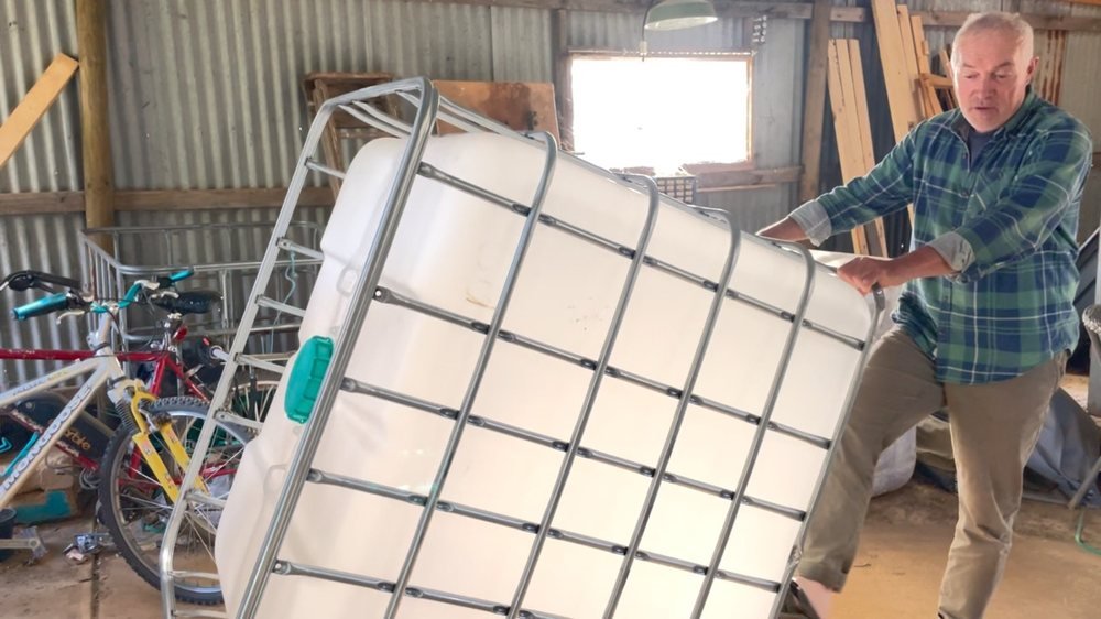 Phil tilting a second-hand IBC tote in its steel cage in a shed, before any work has started on it
