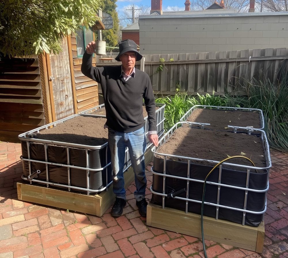Phil standing between two freshly installed wicking beds on a brick paved courtyard, showing their waist height